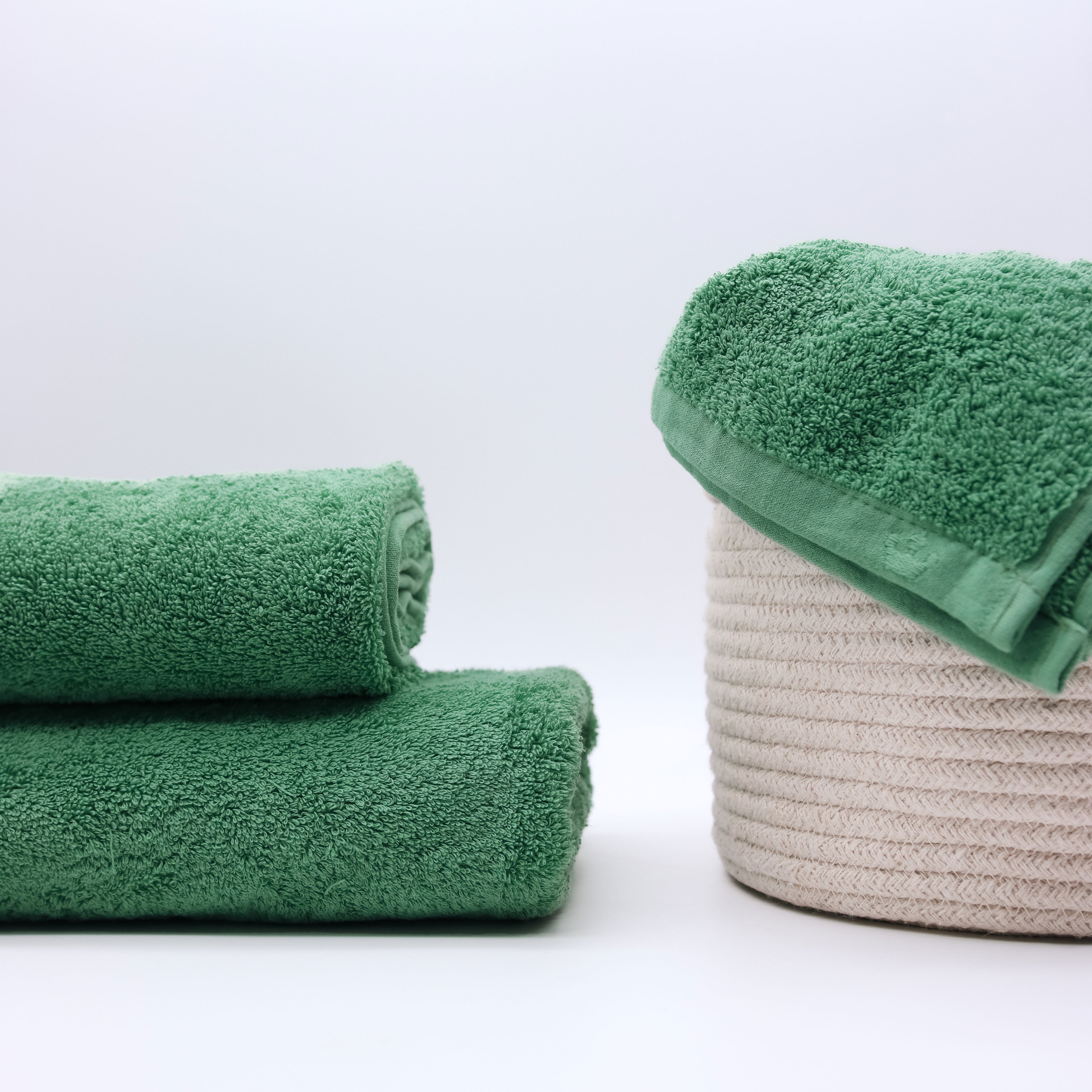 two folded green towel with a beige basket with a green towels inside