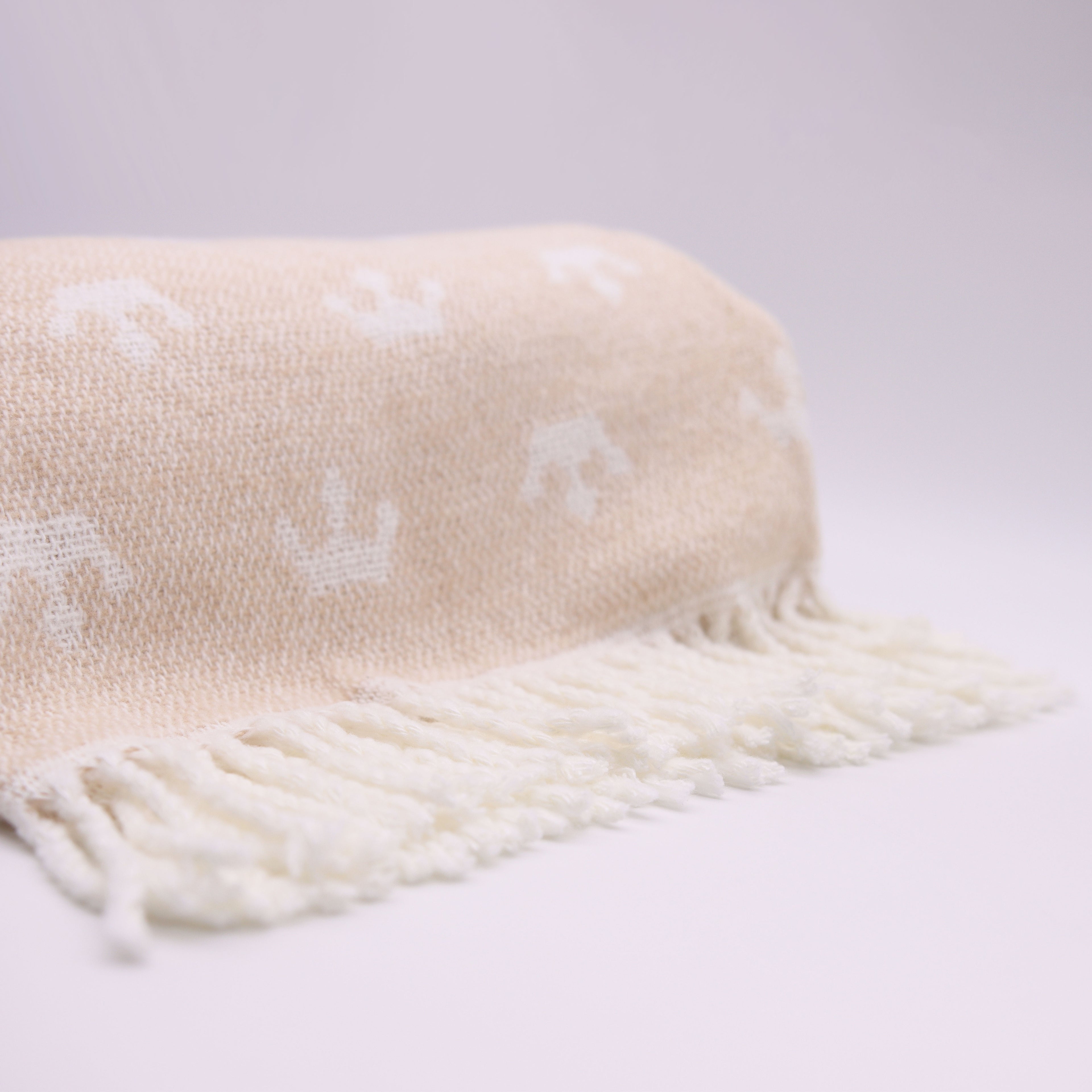 Beige blanket with white fringe and subtle pattern on a light gray background