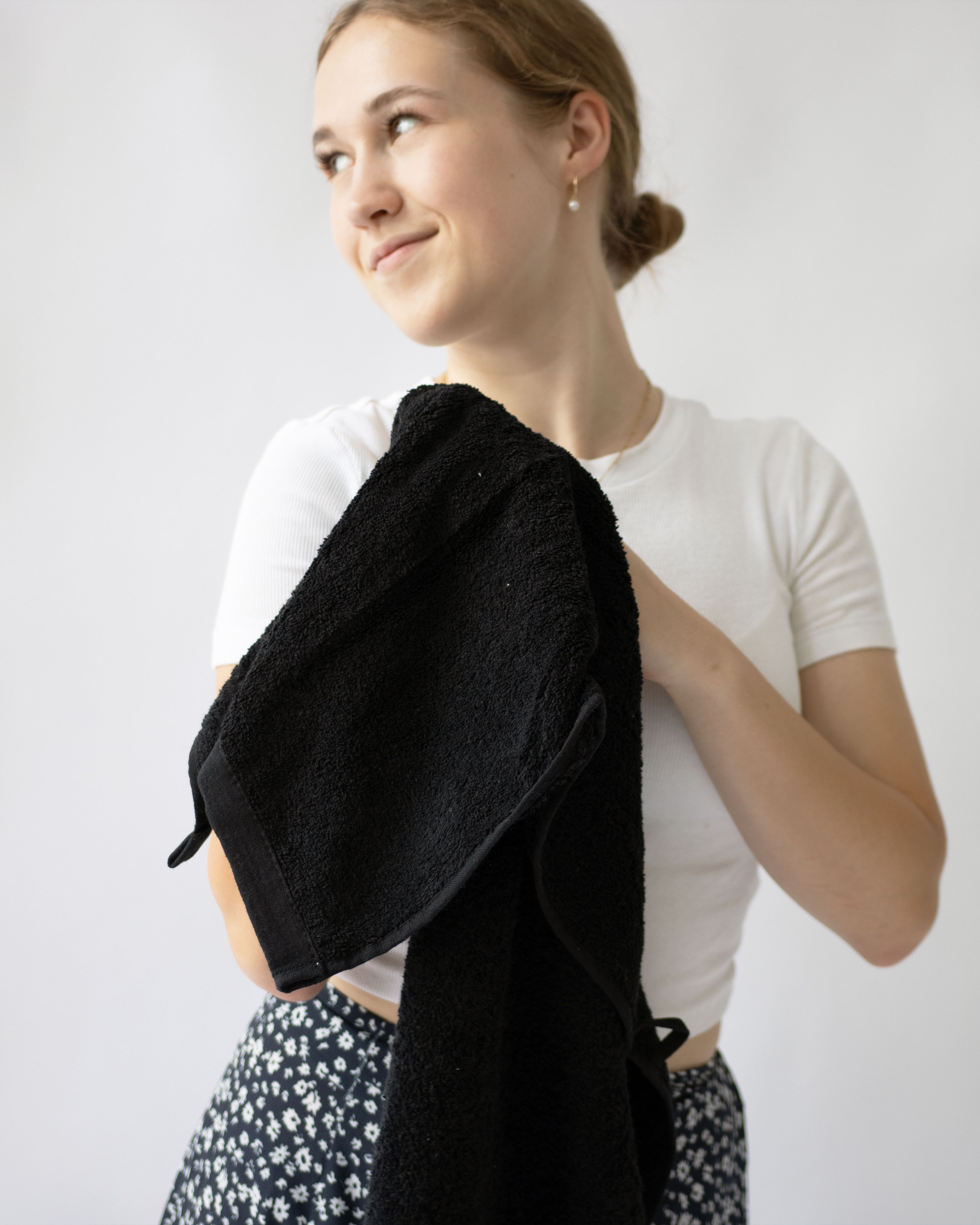 Woman with plain white shirt and blue flowered skirt holding a black towel against a white background