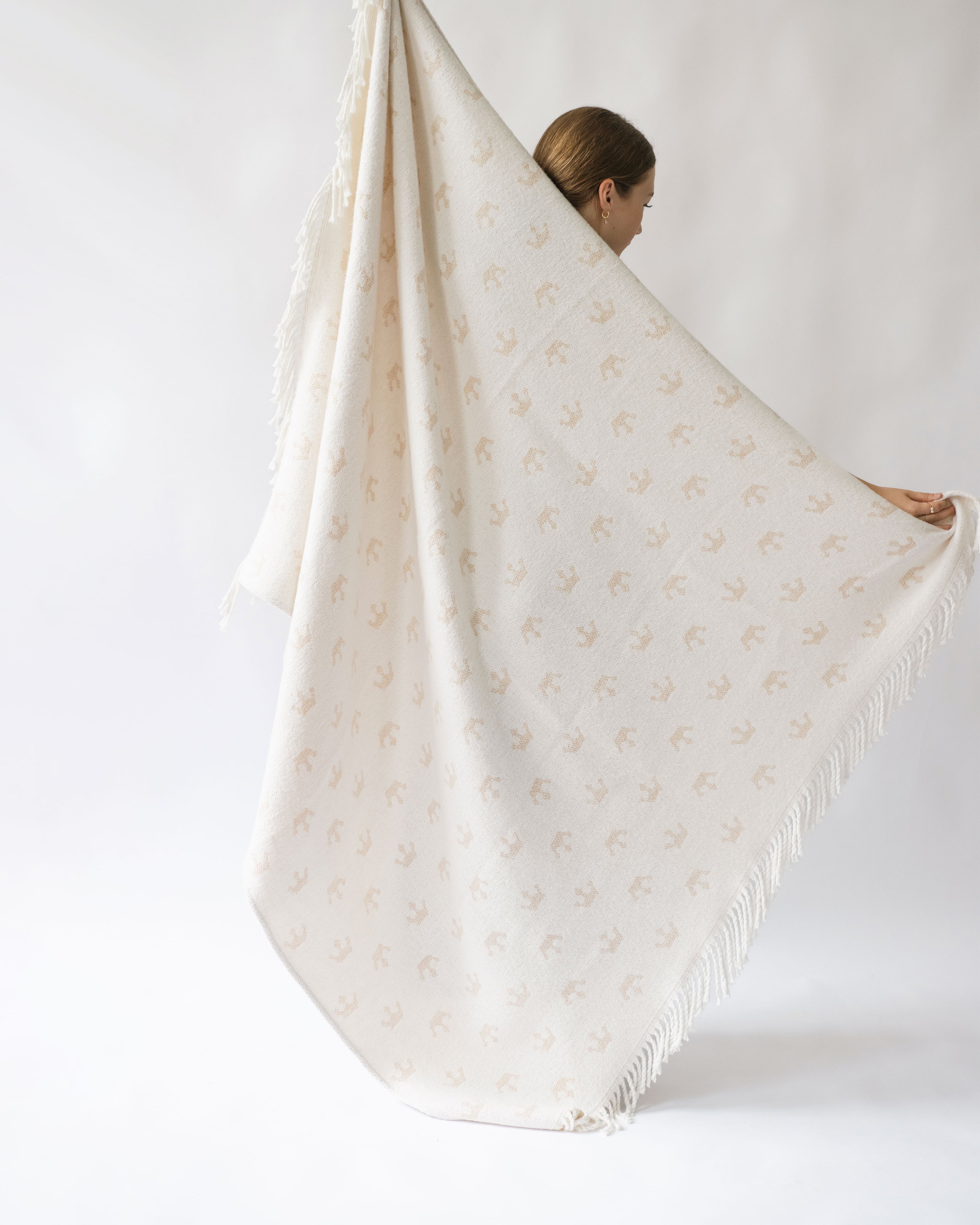 Person holding a large beige blanket with subtle pattern on a white background