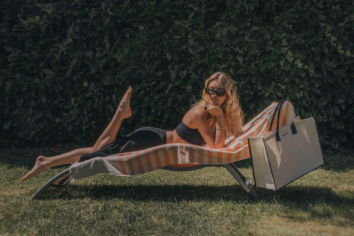 Woman lying on a striped towel with a shopping bag next to her in a park setting