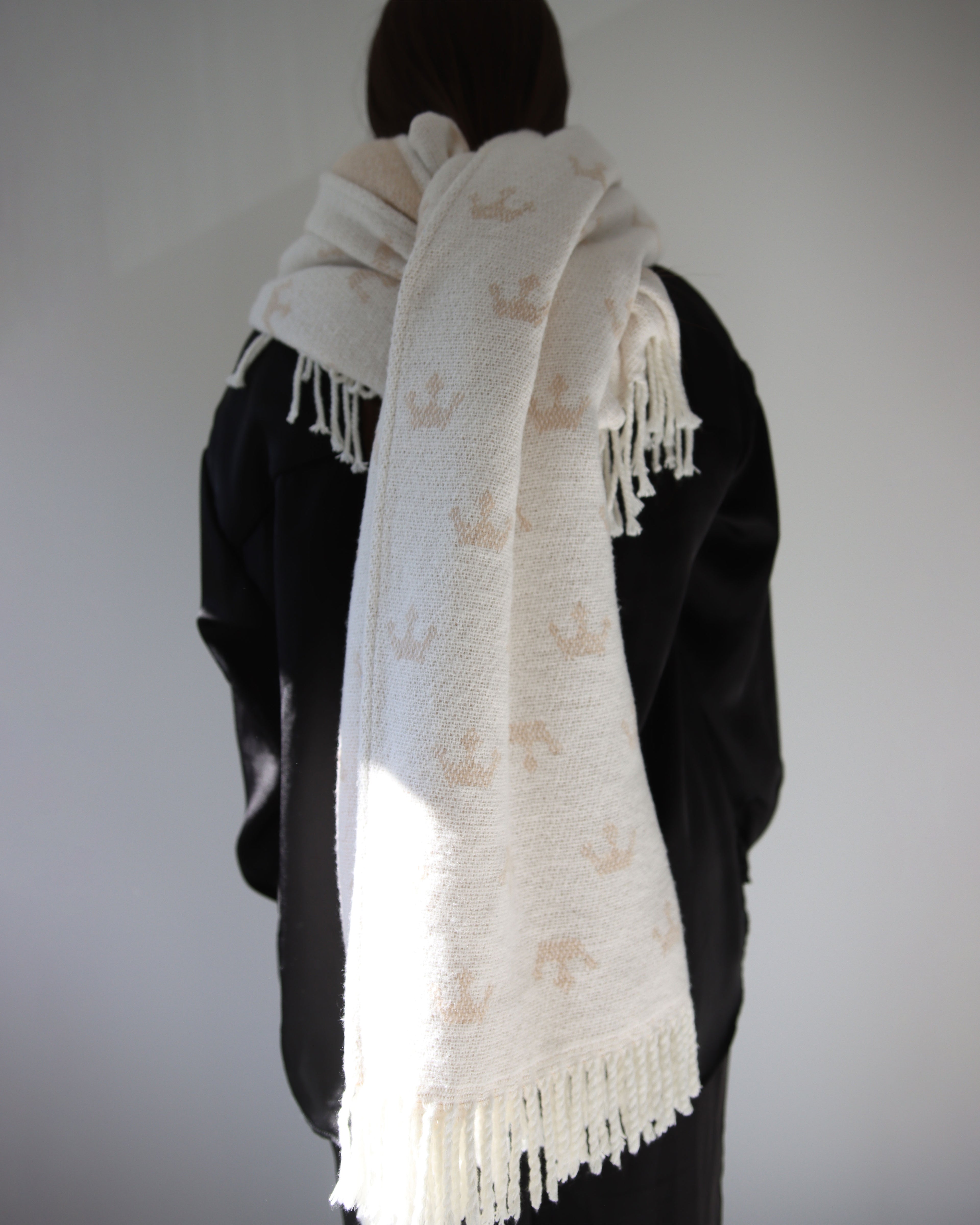 Person wearing a white scarf with gold patterns against a plain background