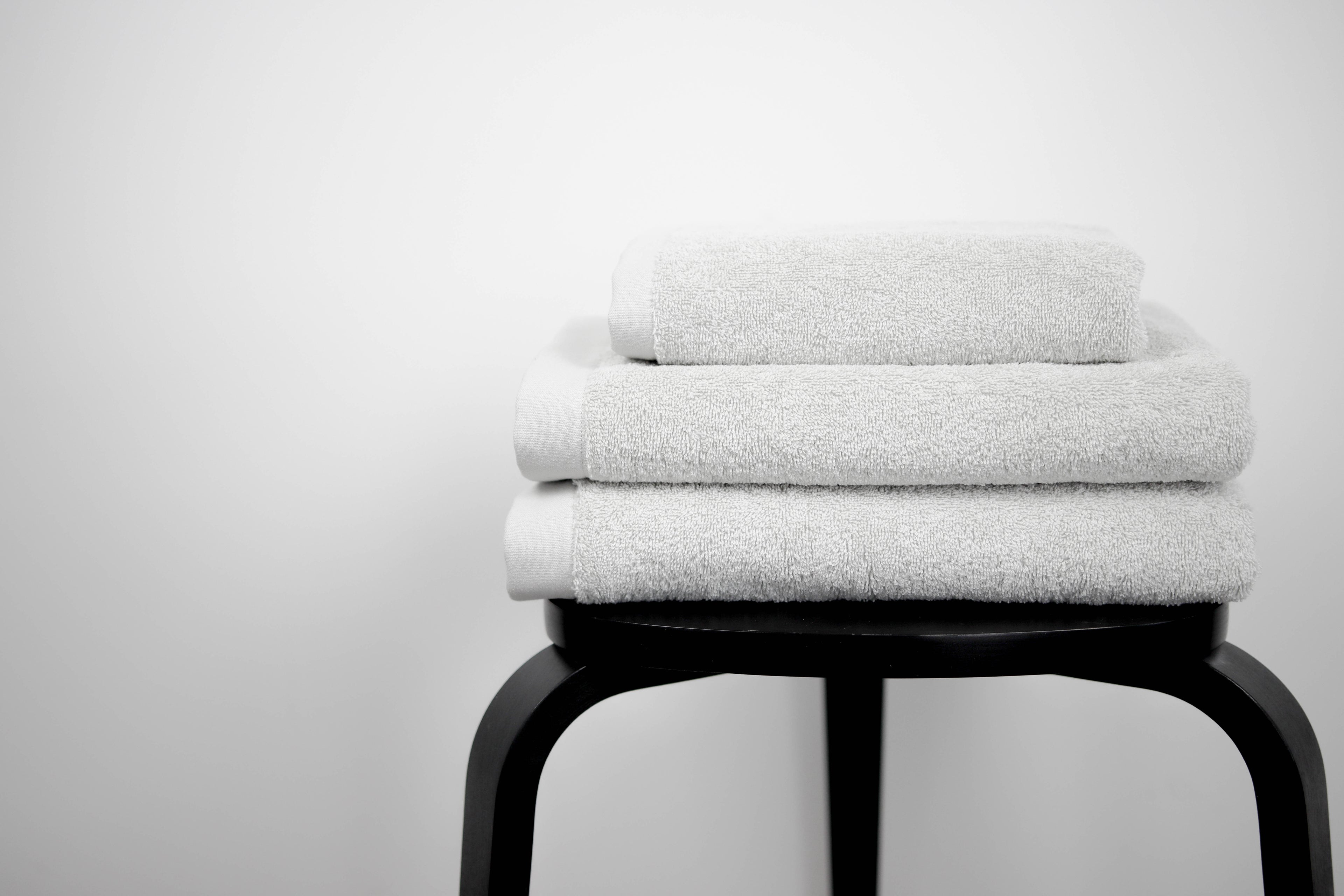 Stack of white towels on a black stool against a light gray background