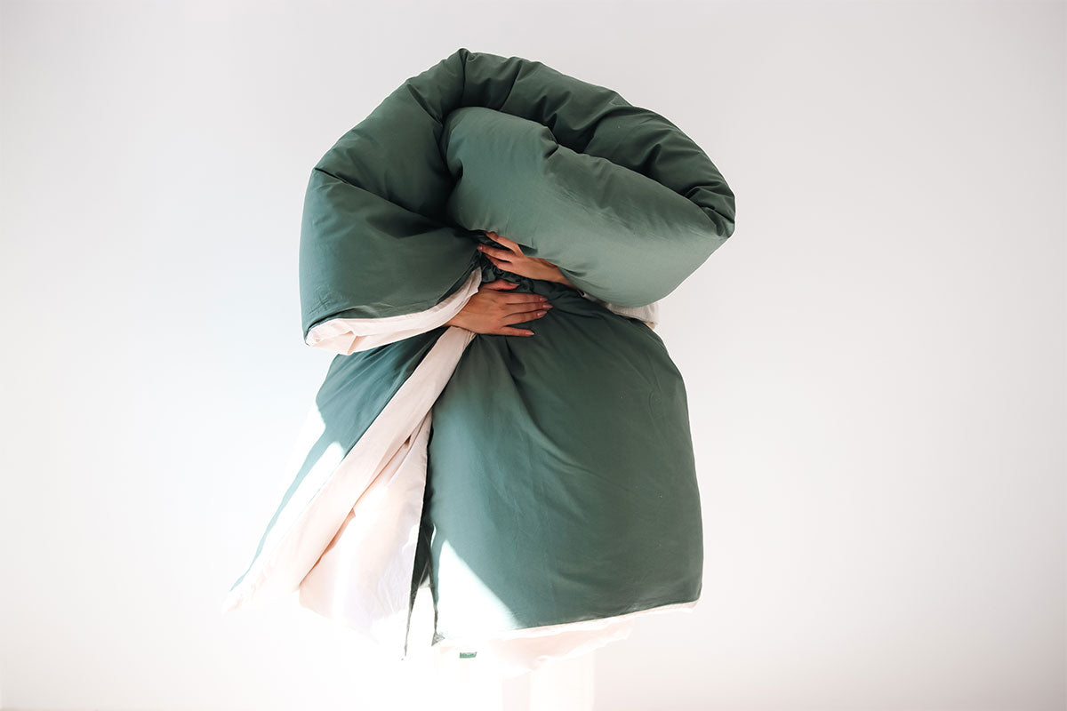 Person holding a large green cotton duvet comforter against a white background