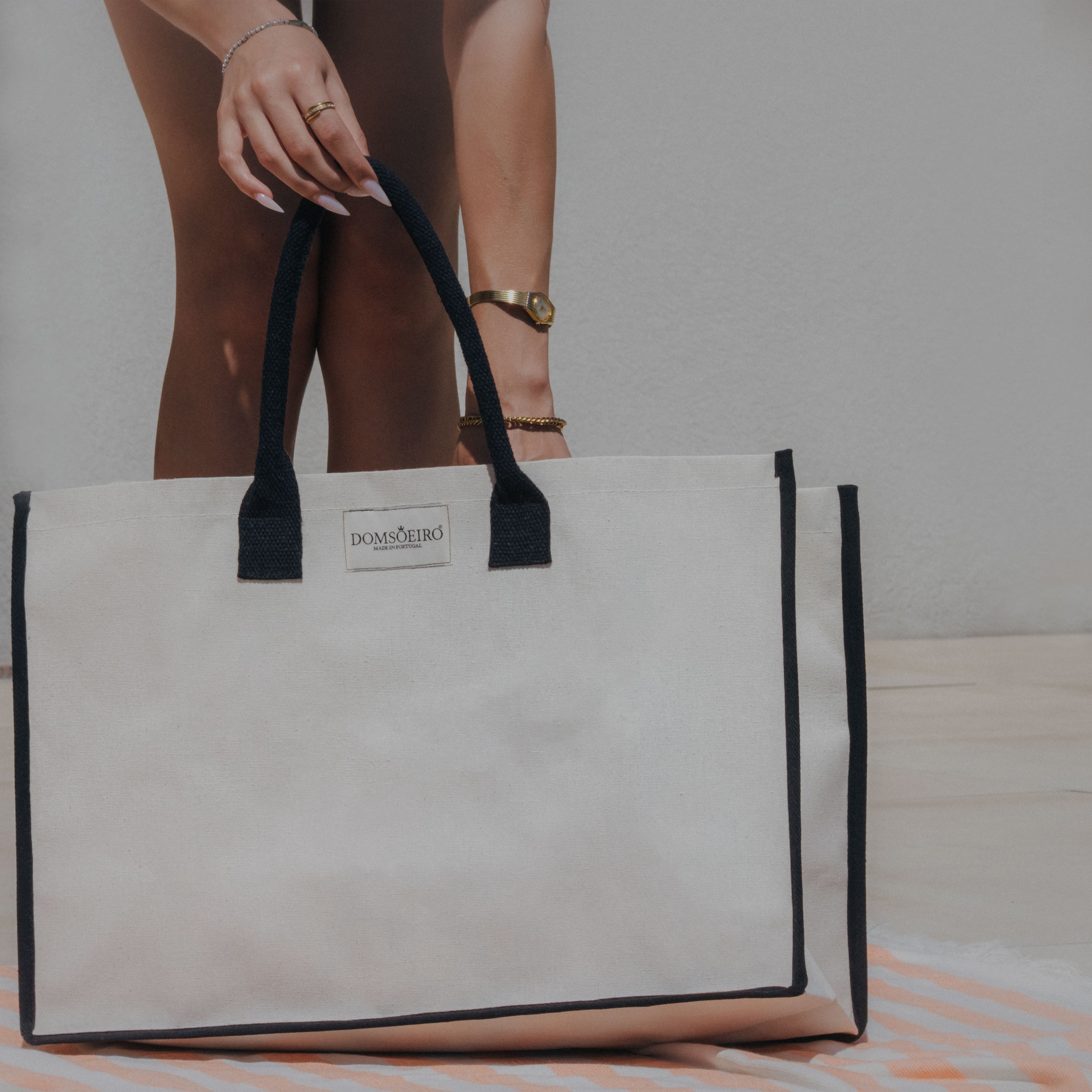 White tote bag with black trim held by a person on a striped surface