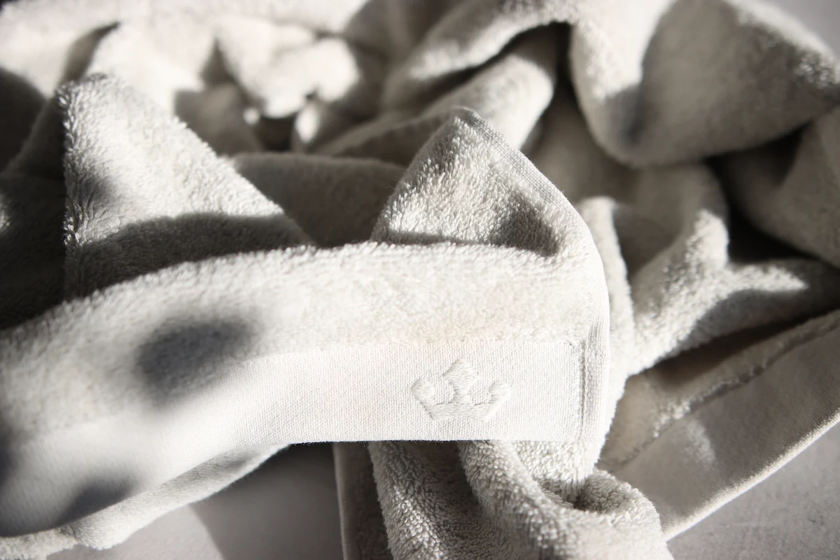Wie Sie Ihr Handtuch ohne Trockner weich halten können - graues Handtuch auf dem Bett, mit Sonnenstrahlen