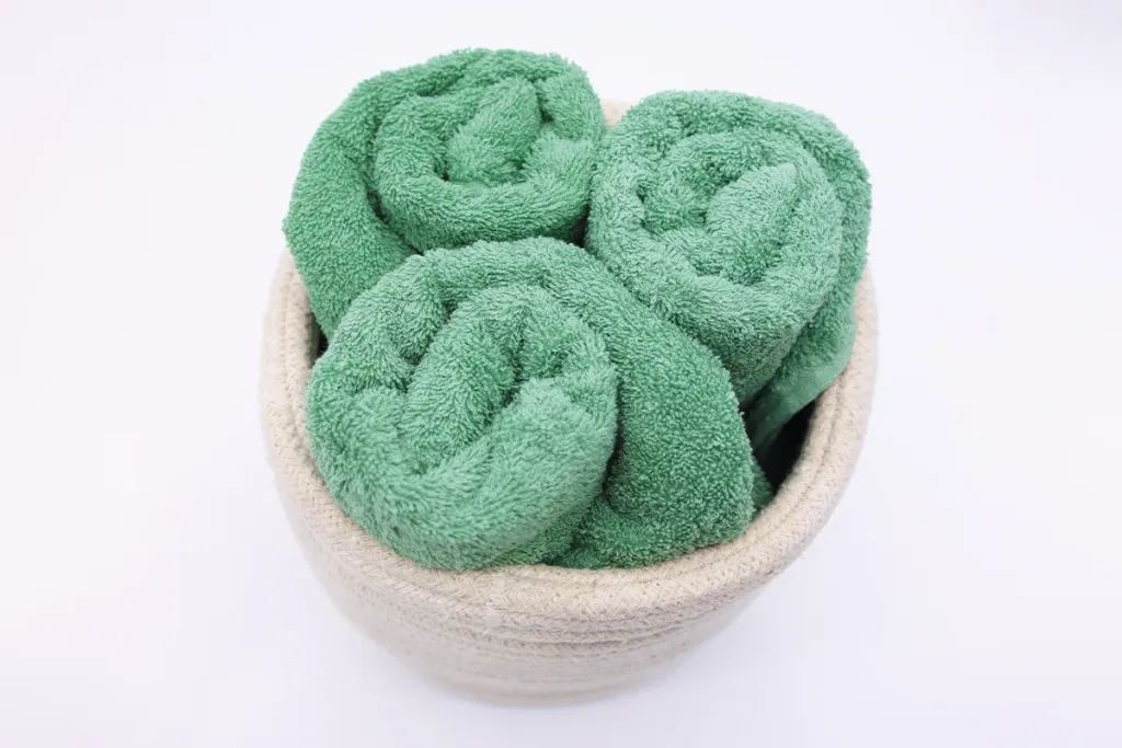 beige textile basket with three rolled jade green towels from domsoeiro
