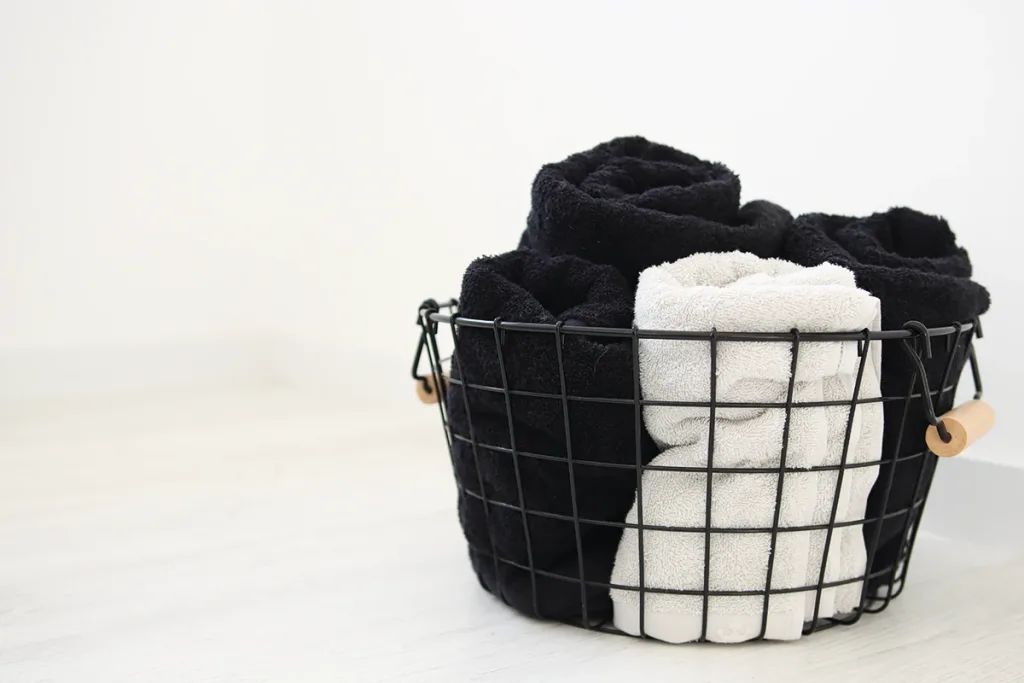 Cesto negro con toallas grises y negras de Domsoeiro en una habitación blanca