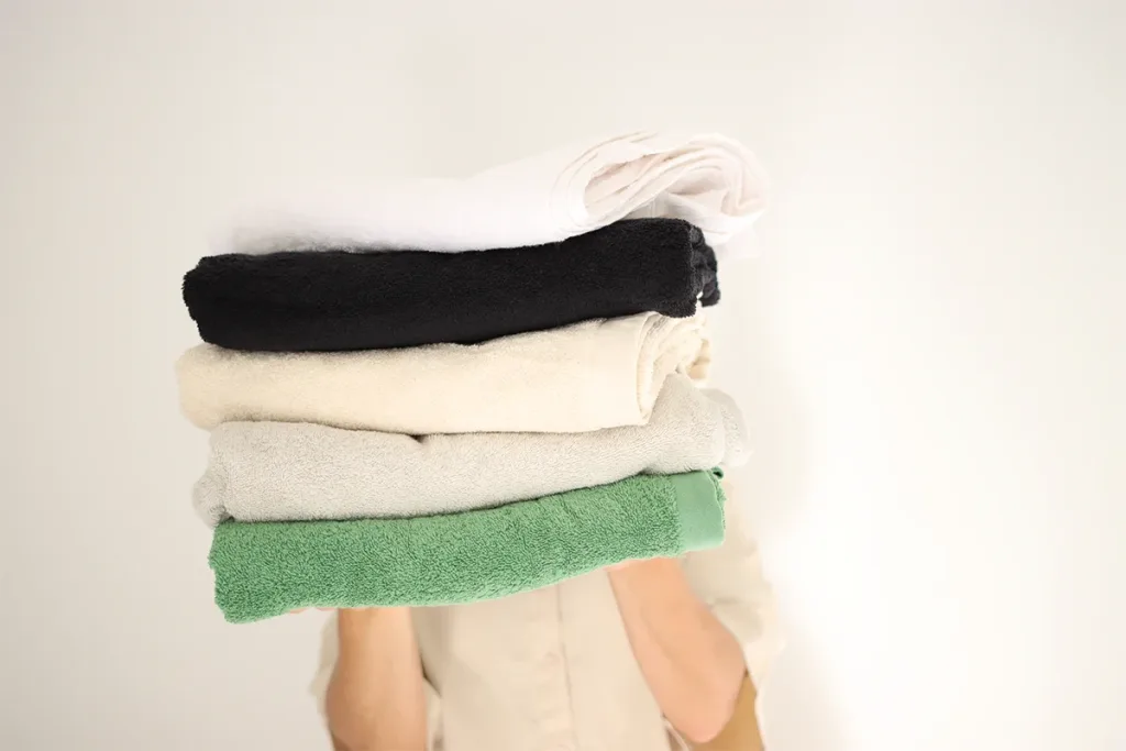 Person in Beige hält fünf verschiedene gefaltete Handtücher in verschiedenen Farben von DomSoeiro.