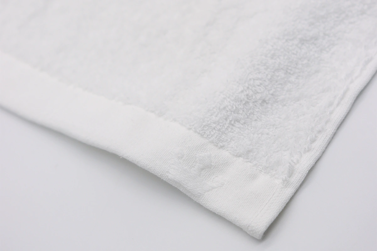 Ecke eines weißen Handtuchs von domsoiero mit eingesticktem Logo