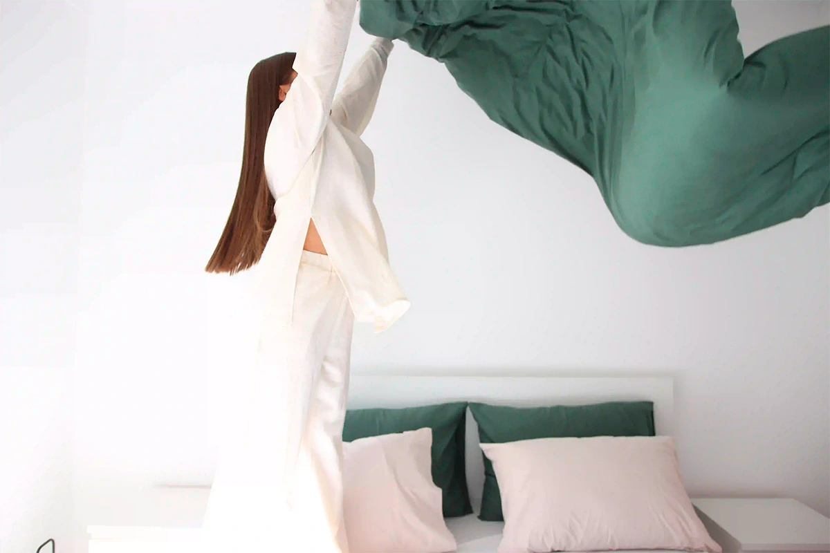 chica lanzando un suave edredón verde oscuro sobre una cama después de cuidar su ropa de cama