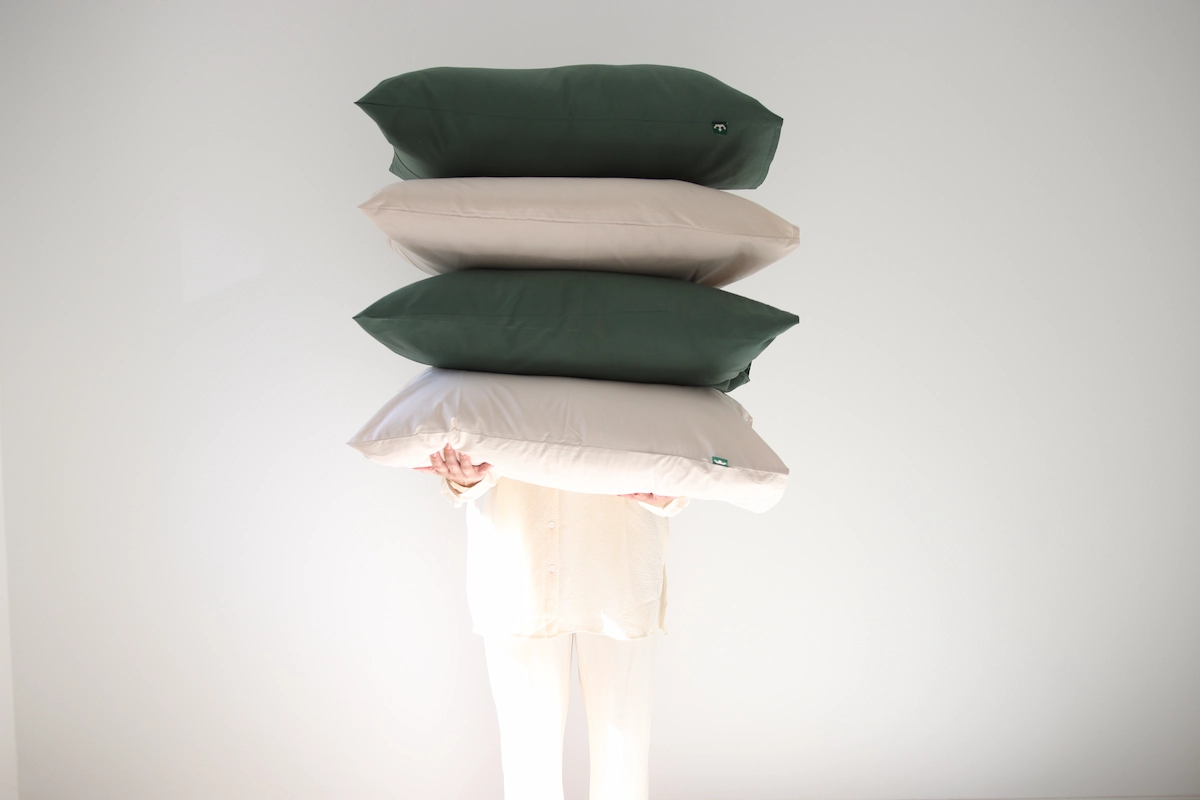 person carrying a bunch of pillows with beige and dark green pillowcases