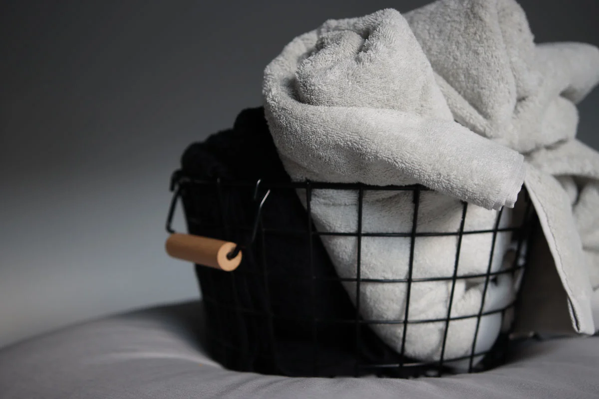 Toallas grises y negras enrolladas en una cesta negra de alambre